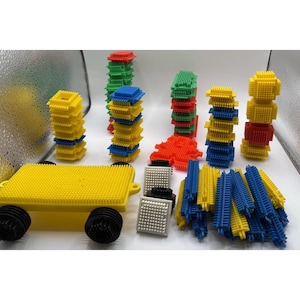 Puede incluir: Un conjunto de bloques de construcción coloridos de varias formas y tamaños. El conjunto incluye una base amarilla con ruedas negras, pilas de bloques amarillos, azules, verdes y rojos, y varias piezas cuadradas y rectangulares más pequeñas. Los bloques están diseñados para encajar.