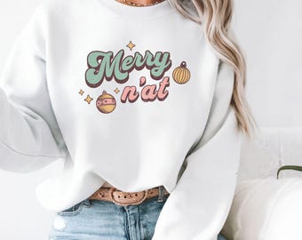 May include: White sweatshirt with the text "Merry n'at" in a retro font, with decorative stars and ornaments. The design features a mint green and pink color scheme, evoking a vintage Christmas aesthetic.