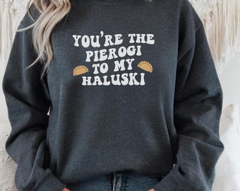 May include: Dark gray sweatshirt with the text "YOU'RE THE PIEROGI TO MY HALUSKI" in white, with two pierogi illustrations. The sweatshirt is a casual style, suitable for everyday wear.