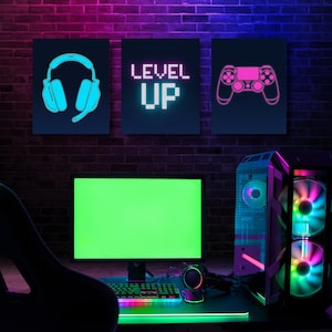 May include: Gaming setup with a green screen monitor, keyboard, and computer tower. Three framed images above display a headset, the words "LEVEL UP", and a game controller. The scene is illuminated with neon lights against a brick wall.