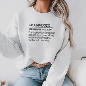 May include: White sweatshirt with the word "GROUNDHOGESE" printed in black, along with a definition. The definition describes the language spoken by a groundhog to announce if winter will continue.