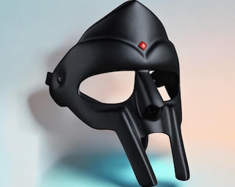 May include: A matte black mask with a distinctive design, featuring a pointed top and a prominent nose piece. A small, red gem is set above the nose. The mask has eye openings and a chin piece. The mask is likely for costume or decorative purposes.