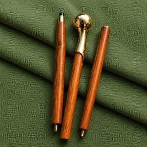 Könnte beinhalten: Ein dreiteiliges Gehstock-Set mit einem polierten goldfarbenen Metallgriff mit kugelförmigem Kopf und zwei braunen Holzsegmenten mit sichtbarer Maserung. Jedes Holzsegment verfügt über ein metallenes Schraubgewinde an einem Ende.