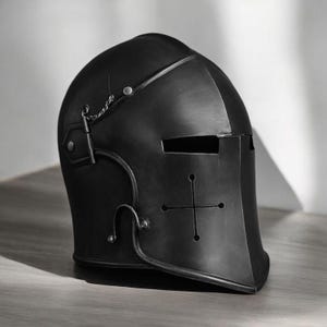 May include: A matte black knight helmet featuring a rounded dome, a horizontal eye slit, and a cross-shaped ventilation cutout on the front face. The helmet includes a small metal chain attachment on the side and silver-toned rivets.