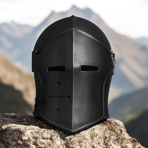 May include: A matte black knight helmet featuring a pointed visor, two horizontal rectangular eye slits, and a cross-shaped ventilation cutout on the lower front section. The helmet includes small metal chain attachments on the sides.