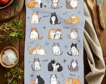 May include: A blue kitchen towel with a white border features a repeating pattern of cute cartoon cats in various poses. The cats are in different colors, including orange, black, white, and gray. The towel has the words "Meow!" and "Purrr!" printed on it.