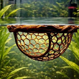 Op de afbeelding: Een bruin aquariumnet met honingraatpatroon, gedeeltelijk ondergedompeld in water. Het net is opgehangen aan een houten rand, met weelderige groene waterplanten op de achtergrond. De afbeelding is een close-up.