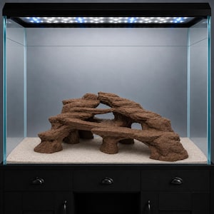 Op de afbeelding: Een rechthoekig glazen aquarium met een zwarte bovenrand en geïntegreerde ledverlichting. Binnenin staat een gestructureerde, bruine rotsachtige decoratie met meerdere niveaus en openingen op een ondergrond van lichtbeige zand.