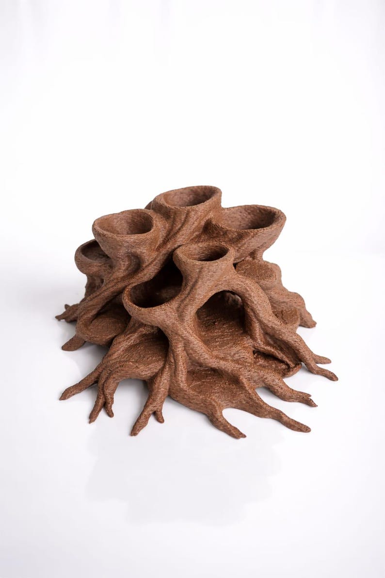 May include: A brown, abstract sculpture resembling a tree with multiple openings. The sculpture has a textured surface and a complex, organic form. The design features multiple cup-like openings and root-like structures extending outwards.