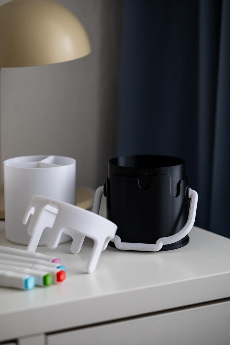 May include: Two white paint can shaped organizers with a white lid and a black paint can shaped organizer with a white lid. The organizers are on a white surface with five colorful markers.