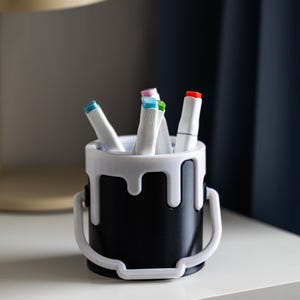 May include: A black paint can shaped pencil holder with white dripping paint detail. The holder is filled with colorful markers.