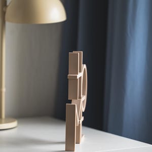 May include: A light beige, three-dimensional wooden sign featuring the word HOME in a block letter font. The letters are connected and stand upright, displaying a smooth, matte finish on all visible surfaces of the individual characters.