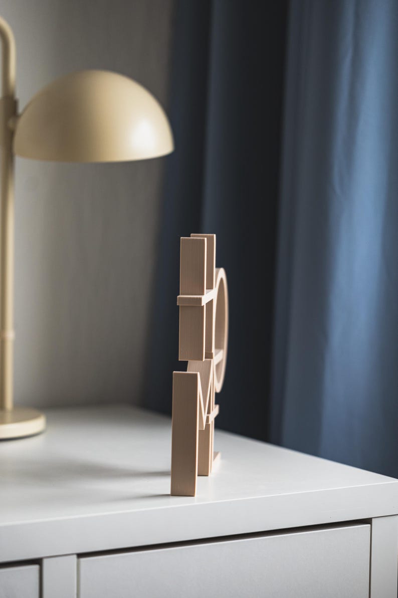 May include: A light beige, three-dimensional wooden sign featuring the word HOME in a block letter font. The letters are connected and stand upright, displaying a smooth, matte finish on all visible surfaces of the individual characters.
