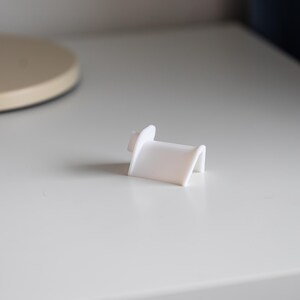 Puede incluir: Soporte para tel&eacute;fono de pl&aacute;stico blanco con un dise&ntilde;o curvo.