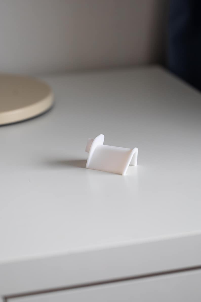 Puede incluir: Soporte para tel&eacute;fono de pl&aacute;stico blanco con un dise&ntilde;o curvo.