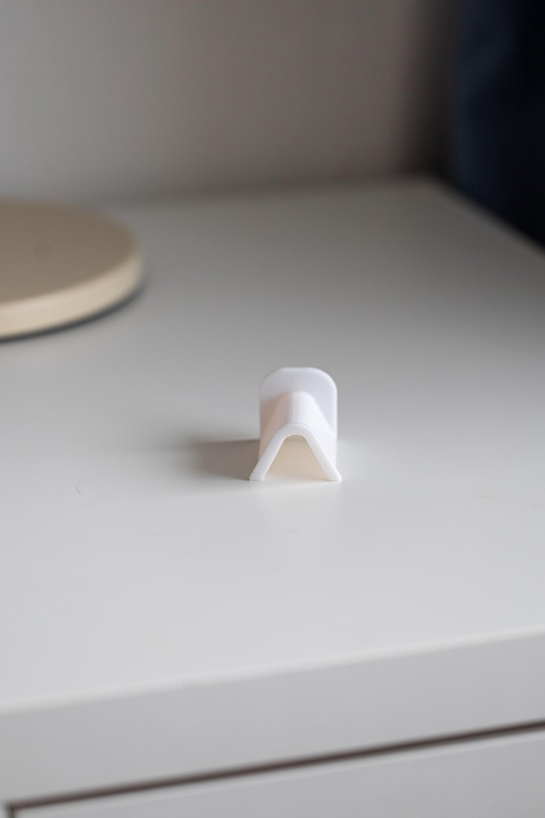 Puede incluir: Soporte para tel&eacute;fono de pl&aacute;stico blanco con forma triangular. El soporte est&aacute; dise&ntilde;ado para sostener un tel&eacute;fono en posici&oacute;n vertical.