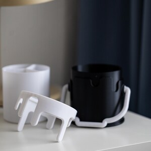 May include: Two white paint can organizers with a drip design. One organizer is upright and the other is laying on its side.