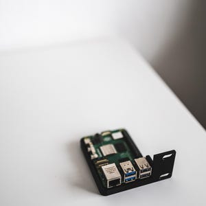 Op de afbeelding: Een kleine, rechthoekige printplaat met diverse poorten en componenten. De printplaat is zwart en groen, met zilveren en blauwe connectoren, tegen een witte achtergrond.