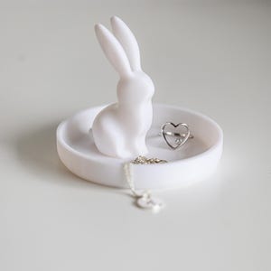 Peut inclure: Un plat &agrave; bagues en c&eacute;ramique blanche avec une figurine de lapin et une bague et un collier en argent en forme de c&oelig;ur.