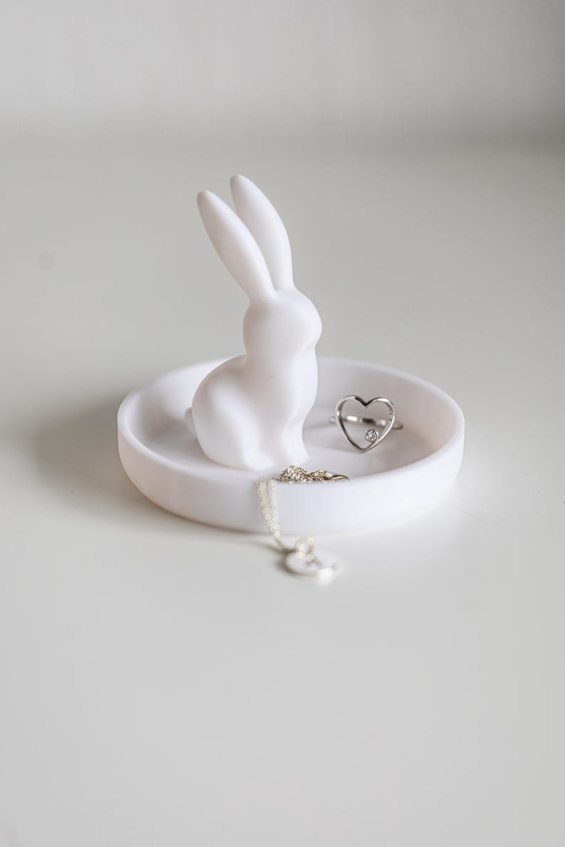Peut inclure: Un plat &agrave; bagues en c&eacute;ramique blanche avec une figurine de lapin et une bague et un collier en argent en forme de c&oelig;ur.