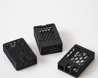 Op de afbeelding: Drie zwarte rechthoekige behuizingen met een honingraatpatroon. De behuizingen zijn gemaakt van een matzwart materiaal en hebben een geometrisch ontwerp. De behuizingen zijn op een wit oppervlak geplaatst.