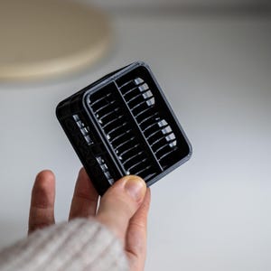 Op de afbeelding: Een zwart plastic 3D-geprint object met een rasterpatroon. Het object wordt in een hand gehouden.