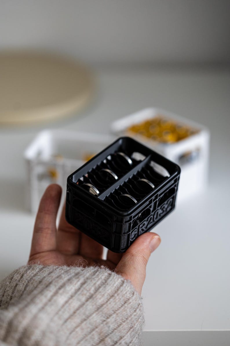 Op de afbeelding: Een zwarte plastic krat met een grijze scheidingswand, met daarin verschillende zilveren ringen. Op de zijkant van de krat staat "GRAUS" gedrukt.