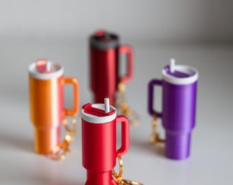 May include: Four colourful travel mugs with lids and straws, three are standing upright and one is sitting down with legs, all with gold keychains.