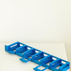 May include: A blue plastic rack with six slots for holding cables or wires. The rack is designed to organise and manage cables.