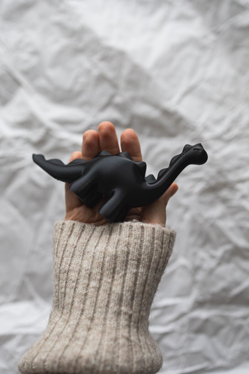 May include: A hand holding a black dinosaur toy. The dinosaur has a long neck and tail.