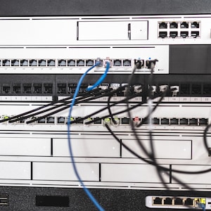 May include: A rack of network servers with multiple ports and cables. The servers are white with black accents and are labeled with the "DIGITUS" brand. Blue and black cables are connected to the servers.