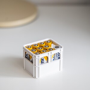 Op de afbeelding: Een witte krat gevuld met gele en blauwe AA-batterijen. De krat heeft een handvat aan de bovenkant en de tekst "Varta Energy" is zichtbaar aan de zijkant.