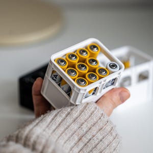 Op de afbeelding: Een witte plastic krat gevuld met gele AA-batterijen. De krat heeft een handvat en is gemaakt om eruit te zien als een mini-melkkrat.