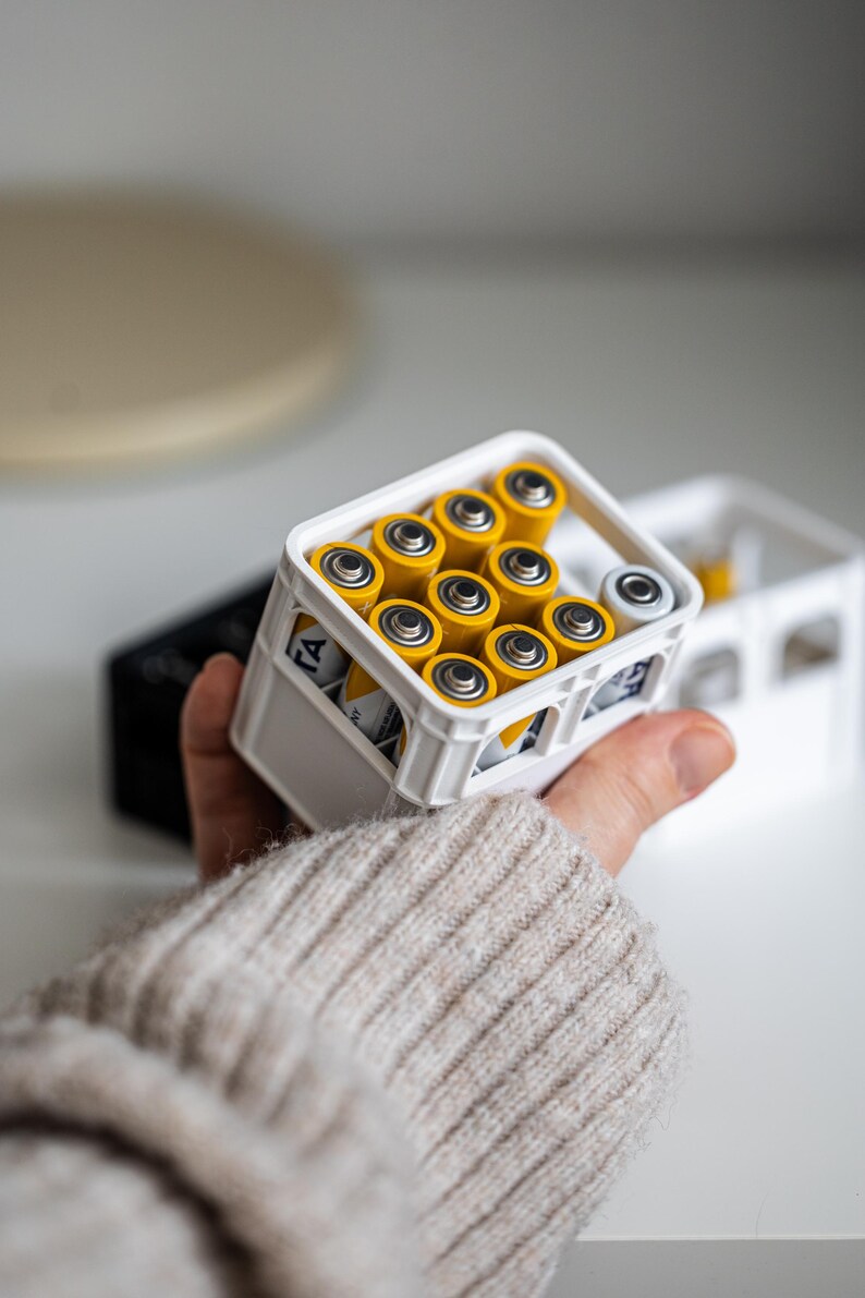 Op de afbeelding: Een witte plastic krat gevuld met gele AA-batterijen. De krat heeft een handvat en is gemaakt om eruit te zien als een mini-melkkrat.