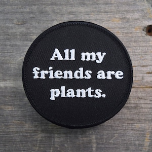 May include: A black round patch with white embroidered text that reads "All my friends are plants."