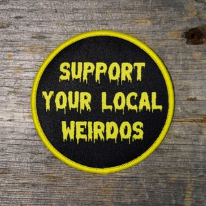 May include: A black and yellow embroidered patch with the text "Support Your Local Weirdos" in a dripping font.