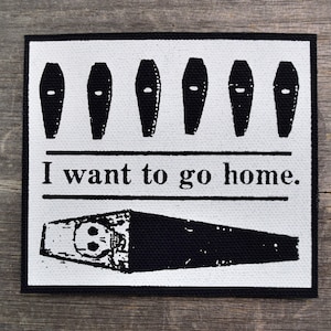 May include: Black and white patch with a row of five coffins and the text "I want to go home."