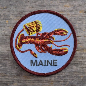 May include: A blue and brown embroidered patch with a lobster and the word "MAINE" on it.