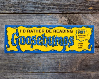 Op de afbeelding: Een rechthoekige gele sticker met een blauwe rand en blauwe tekst die luidt I'D RATHER BE READING Goosebumps. Rechts bevat een kleinere gele tekstballon de tekst FREE TERRIFYING TATTOO en Enter if you dare....