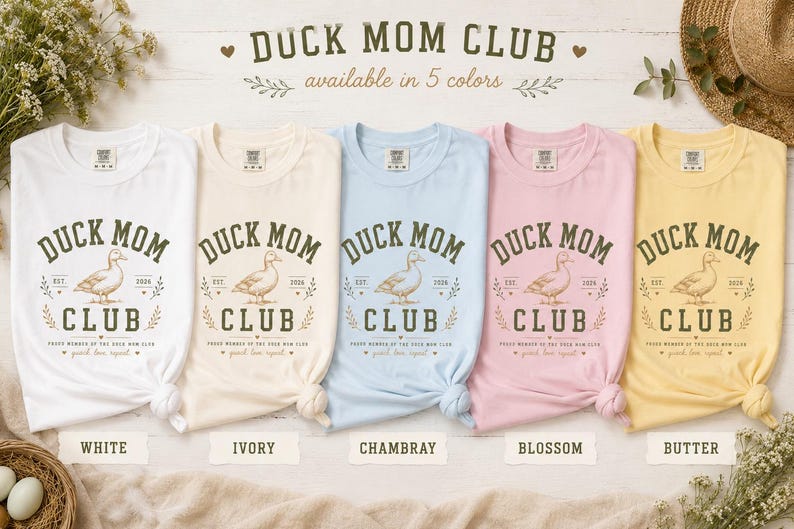 May include: Five t-shirts in white, ivory, chambray, blossom, and butter colors are displayed. Each shirt features the text "DUCK MOM CLUB" with a duck illustration. The text "available in 5 colors" is above the shirts.