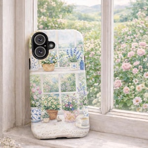 May include: A phone case featuring a watercolor painting of a window with flower pots, a teacup, and a view of a garden. The case is white with a floral design and is resting on a white windowsill.