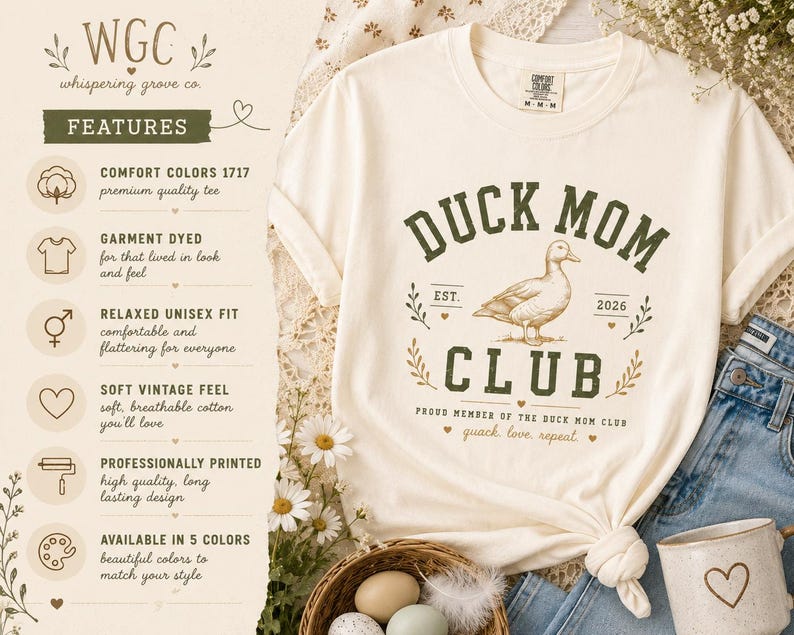 May include: Cream-colored t-shirt with a "Duck Mom Club" graphic in green and brown. The design includes a duck illustration and the words "quack, love, repeat." The shirt has a relaxed, unisex fit.