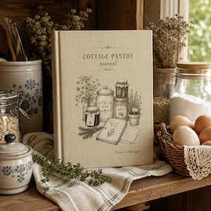 May include: A beige hardback journal titled COTTAGE PANTRY journal by Grace Whitaker. The cover features a detailed black line drawing of pantry items including jars labelled OATS and LEMON PRESERVES, a small book, and herbs.