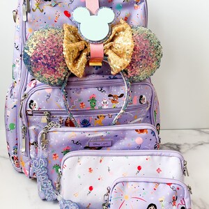 May include: A set of three purple bags with a Disney character print. The largest bag is a backpack with a Mickey Mouse ear headband and a sparkly bow attached. The smaller bags are a cosmetic bag and a small pouch. All bags have a purple and white confetti print with Disney characters like Stitch, Mickey Mouse, and Cinderella.