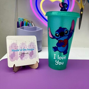Puede incluir: Un vaso reutilizable azul turquesa con acabado brillante presenta un personaje azul Stitch sosteniendo un coraz&oacute;n rojo con el texto "I love you". El vaso tiene una pajita transparente con un personaje azul Stitch en la parte superior.
