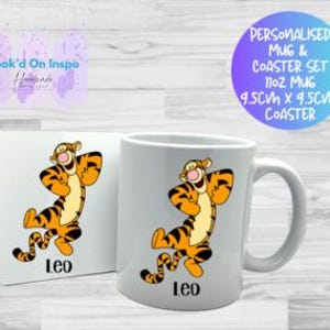 Könnte beinhalten: Ein weißes Keramik-Tassen- und Untersetzer-Set mit einem Cartoon-Tiger-Charakter mit orangefarbenen und schwarzen Streifen. Die Tasse und der Untersetzer sind mit dem Namen "Leo" personalisiert. Die Tasse ist 11 oz.
