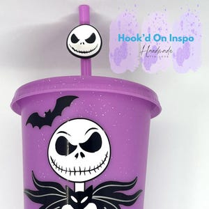 Puede incluir: Un vaso morado con un dise&ntilde;o de Jack Skellington y un adorno de pajita a juego. El vaso presenta un gr&aacute;fico de murci&eacute;lago y el personaje de Jack Skellington. El texto "Hook'd On Inspo Handmade With Love" es visible.