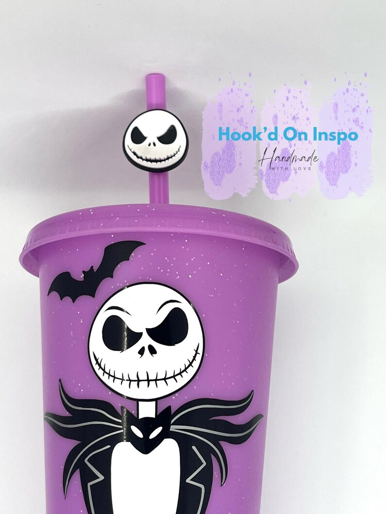 Puede incluir: Un vaso morado con un dise&ntilde;o de Jack Skellington y un adorno de pajita a juego. El vaso presenta un gr&aacute;fico de murci&eacute;lago y el personaje de Jack Skellington. El texto "Hook'd On Inspo Handmade With Love" es visible.