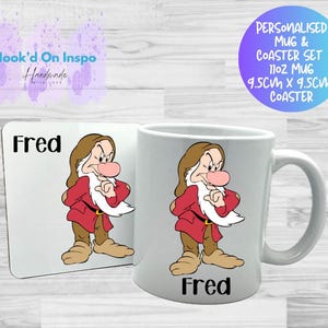 Può includere: Un set personalizzato di tazza e sottobicchiere con un'illustrazione di Fred di Biancaneve. La tazza e il sottobicchiere hanno il nome "Fred" stampato sopra. La tazza è da 11oz e il sottobicchiere misura 9,5 cm x 9,5 cm.