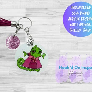 May include: A personalized 5cm round acrylic keyring with a cartoon chameleon in a pink dress. The keyring has a burgundy tassel and a glittery pink charm. Text on the image reads "PERSONALISED 5CM ROUND ACRYLIC KEYRING WITH OPTIONAL TROLLEY TOKEN."